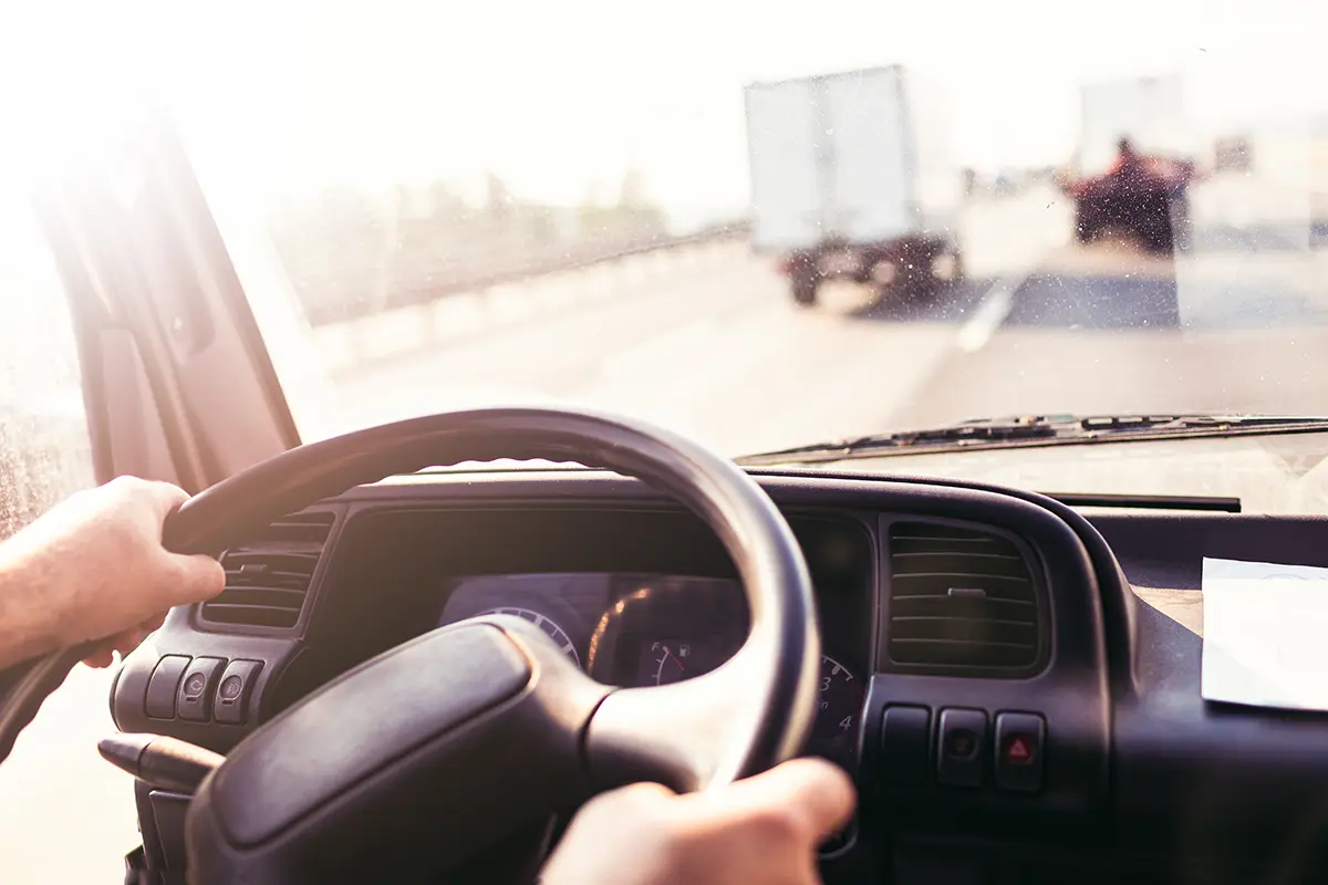 View from inside a vehicle of someone driving on a sunny road, holding the steering wheel, with trucks ahead on the highway—perfect for illustrating carrier vetting in action.