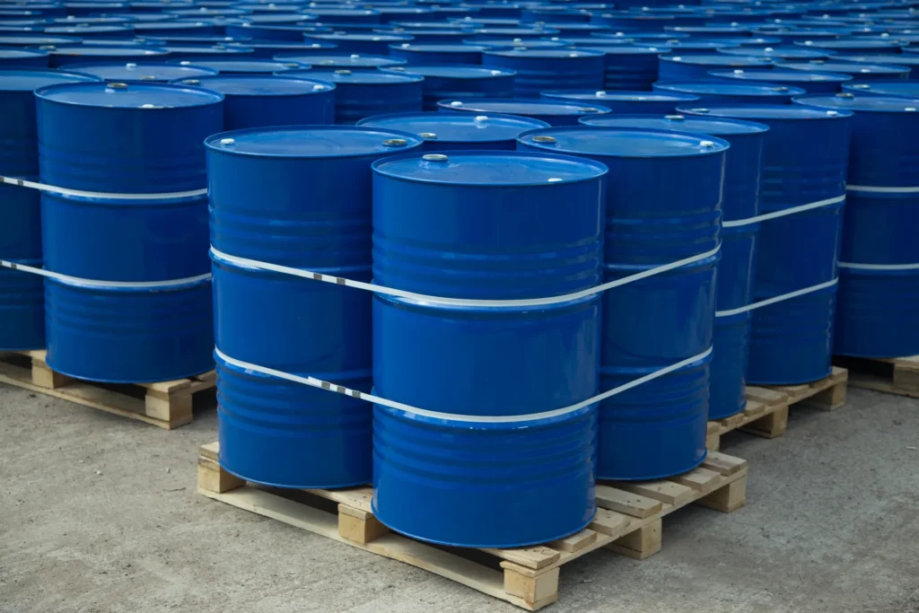 Rows of blue industrial drums sit on wooden pallets. The drums are secured in groups of four with white strapping bands.