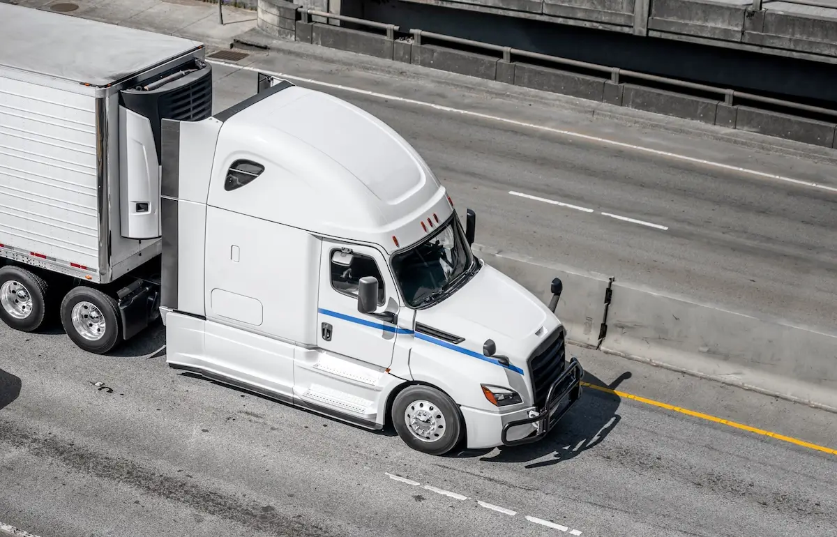 High-angle view of a white semi-truck with blue accents pulling a trailer on a multi-lane highway.